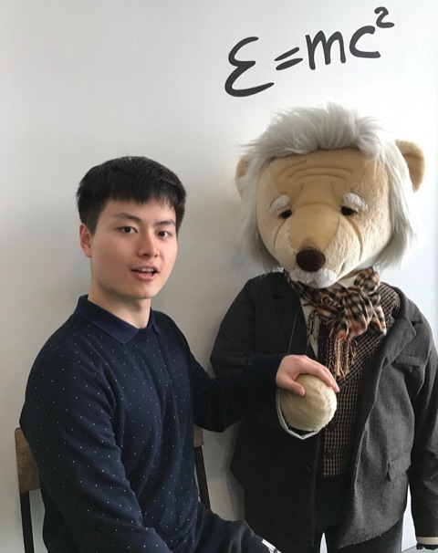 Bo Liu next to an Einstein teddy bear, beneath E = mc² written on the wall